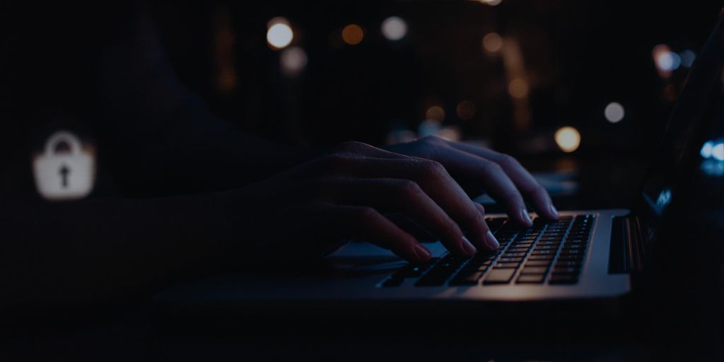Hands typing on a laptop in a dimly lit environment, featuring a padlock icon, symbolizing cybersecurity and data protection strategies.