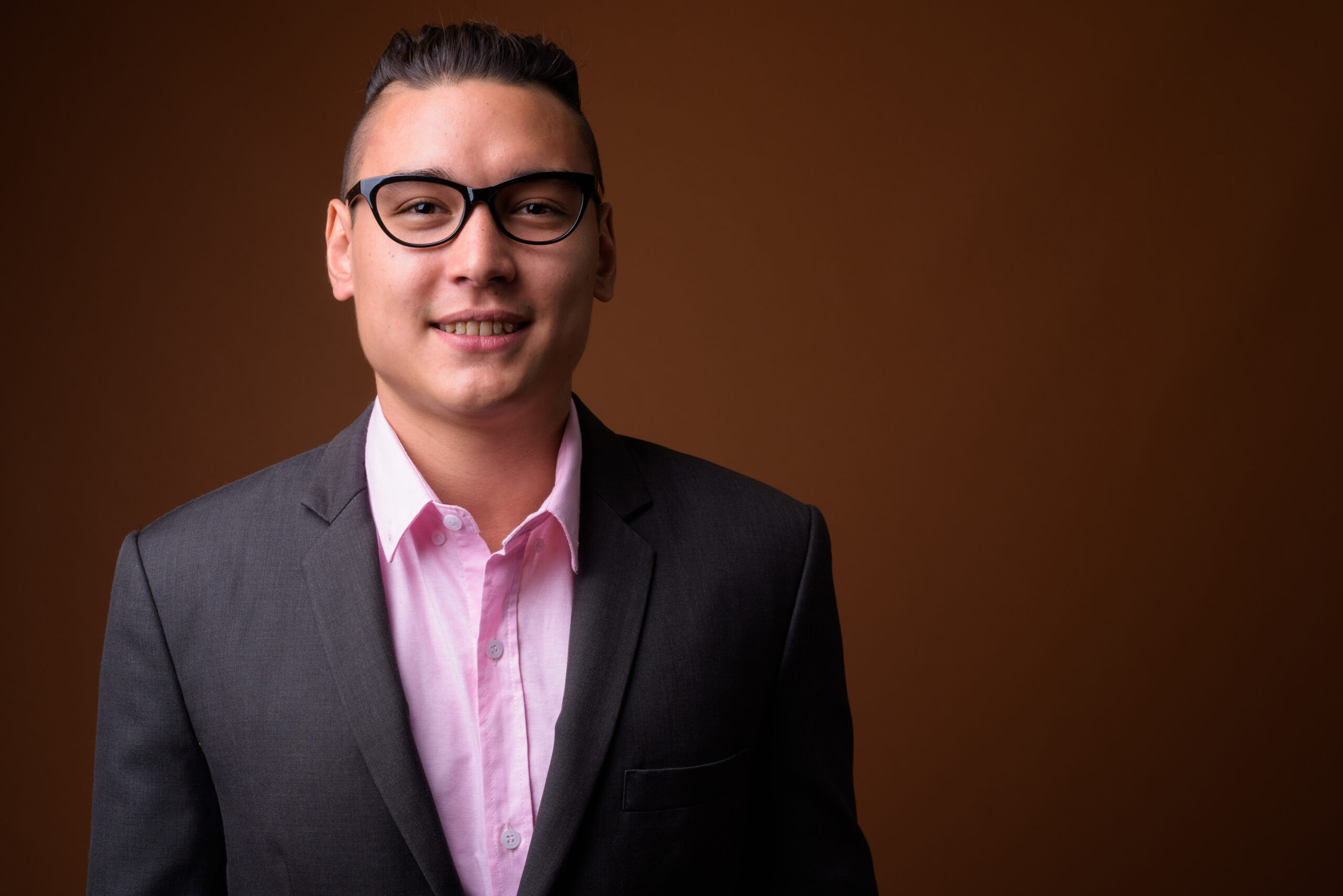 Professional man in a suit and glasses, smiling against a brown background, representing IT support expertise for healthcare practices.